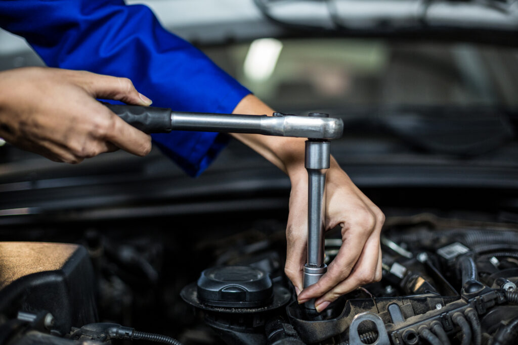 Hands of female mechanic servicing a car in repair garage